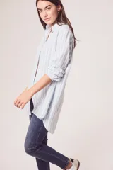Camisa oversize celeste y blanca a rayas verticales, de mangas largas con puños abotonados y cuello camisero.