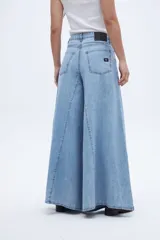 Jean de mezclilla celeste claro, tiro medio, con corte extremadamente ancho y acampanado desde la cadera hasta el bajo, con costuras verticales que acentúan la amplitud de la pierna.