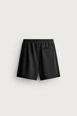 Bermuda estilo jogger de ajuste relajado, color negro, confeccionada en tejido interlock de algodón. Cuenta con cintura elástica ajustable mediante cordón, bolsillos delanteros tipo vivo y diseño liso.