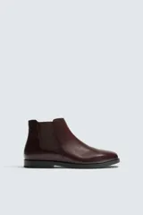 Bota estilo Chelsea de hombre, color marrón oscuro (bordó/vino), fabricada en piel lisa. Presenta elásticos laterales para facilitar el calce y una suela negra de perfil bajo con tacón ligero.