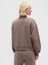 Buzo deportivo de algodón color marrón topo, con cuello alto y medio cierre frontal. Presenta el logo de la marca y el año 1969 bordados en el frente, junto con un emblema circular con un corazón. Posee mangas largas con puños elásticos y un corte holgado.