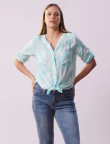 Blusa celeste con estampado blanco, de gasa, con cuello a la base y escote en V. Tiene abertura con botones, bolsillos delanteros y mangas 3/4 regulables con presilla y botón. El ruedo termina con un nudo.