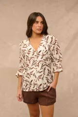 Blusa de cuello en V y cierre frontal con botones, manga 3/4 con volados en los puños, con estampado de hojas marrones sobre fondo beige.