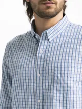 Camisa celeste y blanca a cuadros con cuello abotonado, manga larga y bolsillo en el pecho.