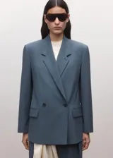 Blazer Uma de corte sastre en color azul acero, confeccionado en mezcla de lana, poliéster y elastano, con forro interior de viscosa. Presenta solapas de muesca, hombreras marcadas, bolsillos con solapa y cierre frontal de doble botonadura.