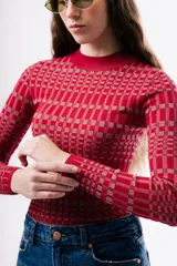 Top de punto ajustado al cuerpo, con cuello redondo y manga larga. Presenta un diseño de estampado geométrico a cuadros en tonos rojos y rosados.