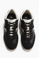 Calzado deportivo con diseño de bloques de color en negro y blanco, con cordones, collarín acolchado y suela de goma.