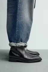 Bota de cuero negro con diseño minimalista, punta fina, cierre lateral con cremallera y tacón bajo.