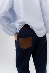 Pantalón de gabardina azul marino, de corte barrel y tiro bajo, con detalles en pana marrón en la pretina y en el ruedo interior vuelto.