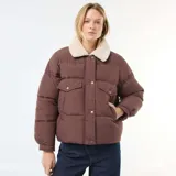 Campera acolchada corta color marrón con cuello de borreguito color crema. Presenta cierre frontal con botones a presión y bolsillos con solapa en el pecho.