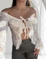 Top de encaje blanco con mangas largas acampanadas, hombros descubiertos, volados y lazo ajustable en el frente.