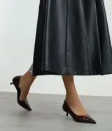 Zapato tipo scarpin con tacón kitten heel, confeccionado en poliuretano con textura símil cuero. Presenta punta fina y un diseño con recorte asimétrico en el empeine.