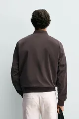 Cazadora bomber ligera de tejido técnico color verde oliva, con cuello, puños y bajo en rib elástico. Presenta cierre frontal de cremallera y bolsillos de vivo en la cadera.