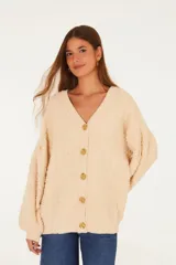 Cardigan largo de punto texturizado color beige, con escote en V, mangas largas voluminosas y cierre frontal con botones dorados con relieve.