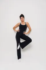 Mono deportivo de una pieza en color negro, con diseño de corte ajustado en el torso y piernas ligeramente acampanadas. Presenta detalles de líneas blancas contrastantes a lo largo de los laterales y en el escote, con espalda estilo nadadora.