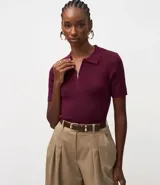 Blusa polo de punto color vino tinto, ajustada al cuerpo, con cuello y manga corta. Presenta una cremallera metálica en la abertura frontal.