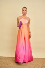 Vestido largo de satén con diseño degradado en tonos salmón y fucsia. Presenta cuello halter con detalle de nudo, falda evasé con tajo frontal pronunciado y espalda descubierta.