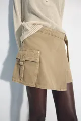Falda pantalón cruzada de tiro medio en color tostado, con diseño estilo cargo que incluye bolsillos de parche con solapa y detalle de argolla metálica. Cuenta con trabillas y un cinturón integrado con hebilla metálica.