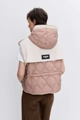 Chaleco reversible con capucha, diseño acolchado con costuras onduladas, cierre frontal y bordes en contraste. Presenta un lado en tono rosado y el otro en tono beige.