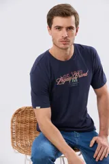 Remera azul marino de manga corta con cuello redondo, confeccionada en mezcla de algodón y poliéster. Presenta un diseño en el frente que combina estampa y bordado con la leyenda "Legacy Brand 1972" en tonos rosado, verde y marrón.