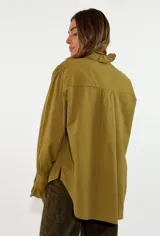 Camisa de algodón color blanco, con cuello redondo y detalle de volados en el cuello y puños. Presenta mangas largas con puños elásticos y un diseño de corte holgado con ruedo asimétrico, más largo en la parte trasera.