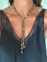 Corbatín estilo lazo elaborado con cuentas de nácar teñidas, discos de piedra hematite en tonos dorados y plateados, y mostacillas. Presenta un diseño de caída central y cuenta con cadena de acero quirúrgico ajustable.