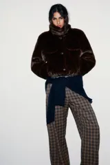 Abrigo corto tipo bomber con textura de pelo sintético, cuello subido, manga larga y cierre frontal con botones. Presenta bolsillos decorativos con solapa en el frente.