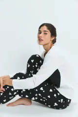 Pijama compuesto por una remera de manga larga blanca y un pantalón negro con estampado de corazones blancos. El pantalón cuenta con cintura elástica para mayor comodidad.