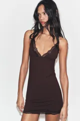 Vestido mini negro con escote en pico y tirantes finos ajustables. Presenta detalles de encaje combinado a tono en el escote y en el ruedo.
