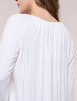 Blusa de modal y elastano color blanco, de silueta holgada, escote redondo amplio con elástico interno fruncido y mangas largas fluidas con puños ajustados.