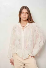 Camisa blanca de manga larga con bordados florales y detalles de ojales, cuello camisero y cierre frontal con botones ocultos.