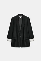 Blazer negro de lino con cuello solapa, manga larga con vuelta a rayas y cierre frontal de un botón. Cuenta con bolsillos delanteros con solapa.