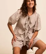 Blusa de tricolina de algodón con estampado de cuadros vichy, mangas cortas abullonadas, cuello redondo, abertura delantera con lazos y recorte fruncido en la cintura.