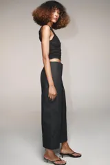 Pantalón marrón de tiro alto con bolsillos delanteros y traseros. El bajo está acabado con vuelta. Cierre frontal con cremallera y ganchos metálicos.