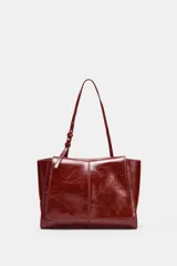 Bolso formato mini shopper de piel con acabado brillante y efecto arrugado. Cuenta con doble compartimento, cierre mediante botón imantado, bolsillo interior y asa de hombro ajustable.