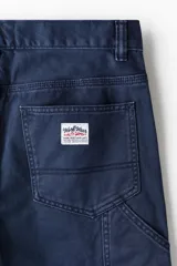 Pantalón carpenter en sarga de algodón gruesa con cintura clásica y cierre con botón. Modelo con bolsillos al bies, bolsillos traseros y piernas rectas con costuras visibles sobre y bajo las rodillas. Cuenta con trabilla funcional en una pierna y bolsillo cargo con doble compartimento en la otra. Corte estándar para una silueta clásica y cómoda.
