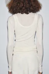 Camiseta blanca de cuello alto y manga larga con detalle de superposición de musculosa a tono. Presenta un corte entallado y está confeccionada con una mezcla que incluye lana.