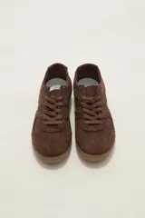 Zapatillas de estilo urbano color chocolate, confeccionadas en material textil tipo gamuza, con cordones al tono y suela de goma plana.