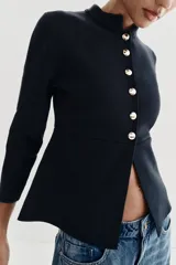 Chaqueta de punto color negro con cuello redondo, manga larga y cierre frontal con botones dorados. Presenta un corte entallado con bajo en evasé.