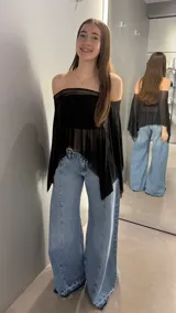 Top tipo capa de tul negro con diseño off-shoulder y corte asimétrico. Presenta una caída fluida y transparente, ideal para superposiciones.