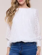 Blusa blanca de organza con textura devoré floral, silueta semiholgada y forro interno. Tiene escote bote, mangas largas abullonadas con transparencias, puños anchos con botones y ruedo elastizado.