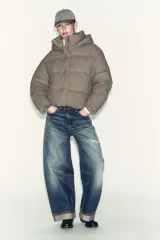 Campera puffer corta de tejido engomado resistente al viento, con aislamiento térmico. Presenta cuello subido con capucha, manga larga, bolsillos delanteros y bajo ajustable con stoppers laterales. Cierre frontal con cremallera termosellada y botones magnéticos.