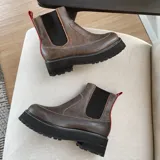 Botas negras de cuero estilo chelsea, con suela track gruesa y elásticos laterales. Presentan una tira vertical de cuero marrón en la parte posterior.
