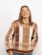Campera de punto con diseño a cuadros tartán en tonos marrones y beige. Presenta un corte oversize, cierre frontal con cremallera, cuello tipo babero con volados y mangas largas con puños ajustados.