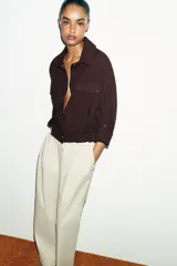 Chaqueta corta marrón de cuello solapa y manga remangada por debajo del codo. Presenta bolsillos delanteros de plastrón con solapa, bajo ajustable con cordón interior y cierre frontal con botones.
