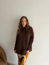 Buzo de punto en color beige, con diseño de trenzas verticales en el frente, cuello redondo y mangas largas con puños acanalados.