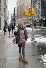 Buzo oversized de punto color tostado con diseño gráfico frontal en azul inspirado en una estampilla con una sirena y el texto 'Taormina'. Presenta tajos laterales, cuello redondo y terminaciones en contraste de color azul.