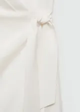 Vestido corto de tejido fluido en color blanco, con escote cruzado, diseño sin mangas y cierre lateral con lazo.