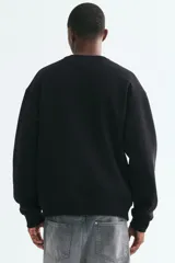 Buzo de mezcla de algodón en color negro, con cuello redondo, hombros caídos y puños y bajo acanalados.