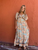 Vestido largo de seda con estampado paisley en tonos naranja, azul y beige. Presenta escote en V, mangas cortas fluidas y falda con volado en el ruedo.